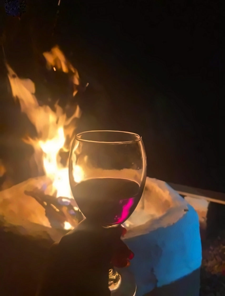 Copa de vino junto a la fogata en una noche de glamping