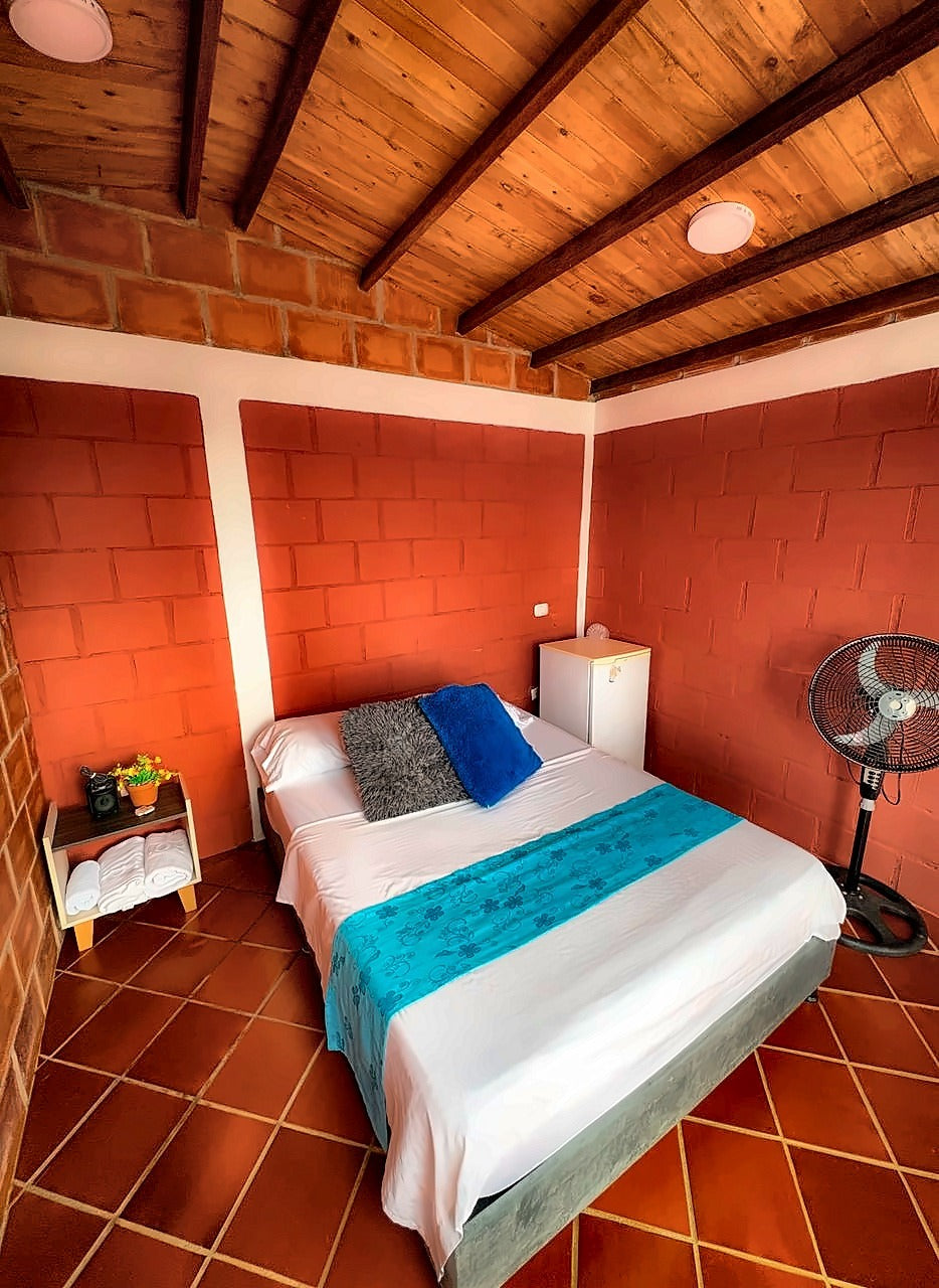 Habitación con cama doble, techo de madera y paredes de ladrillo en Glamping Clavellinas